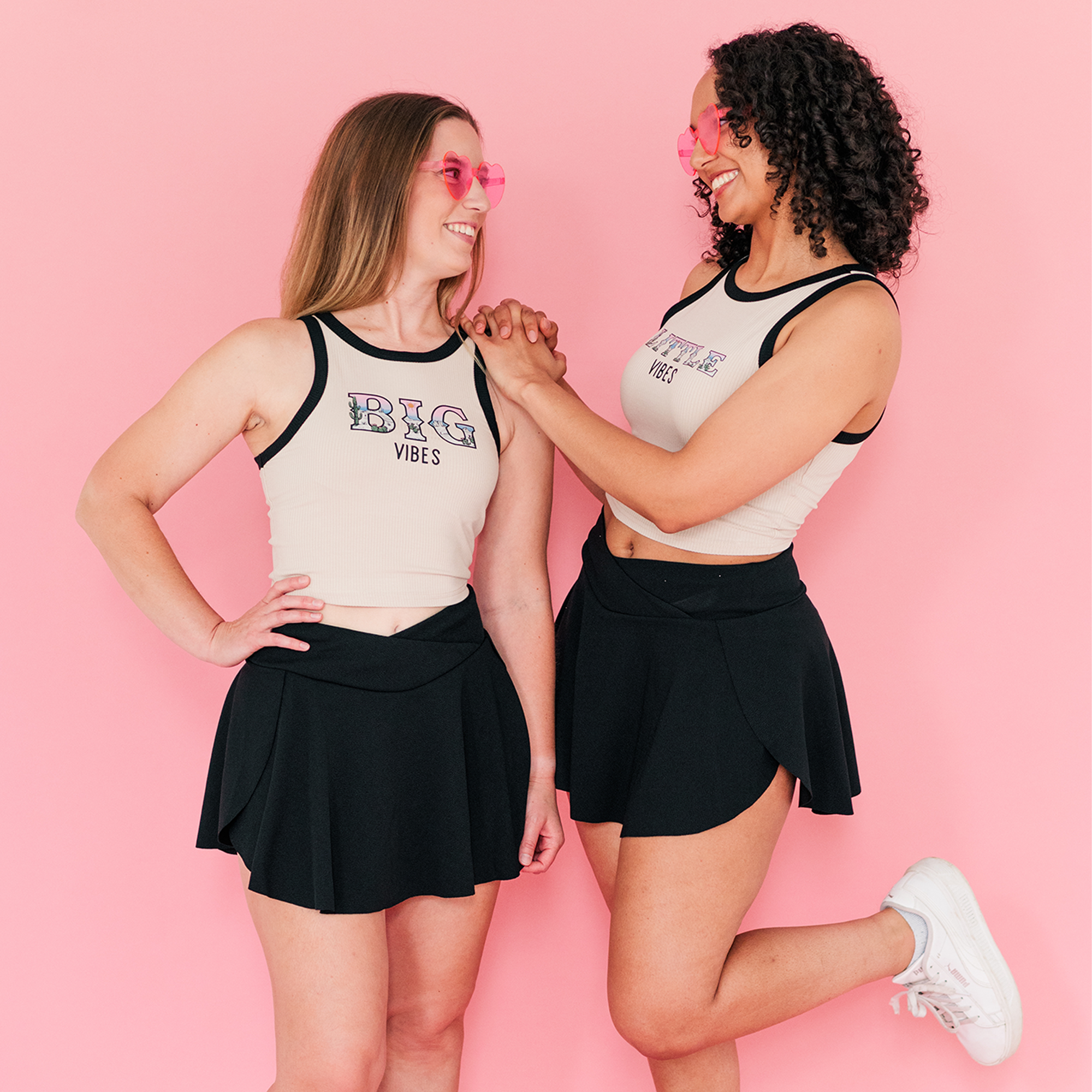 two young women standing next to each other in front of a pink background