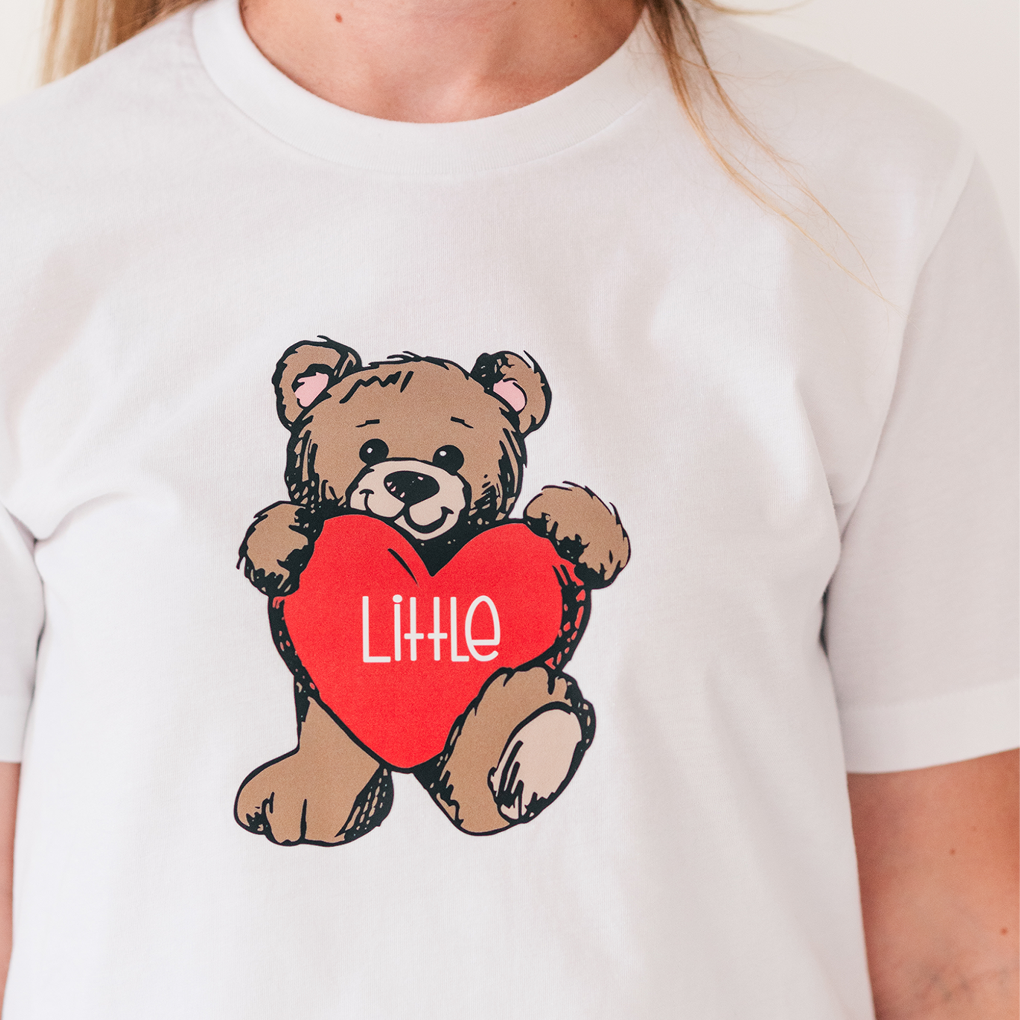 a woman wearing a t - shirt with a teddy bear holding a heart